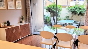 Un comedor con mesa y sillas, un armario de madera y vista al jardín exterior por puertas de vidrio.