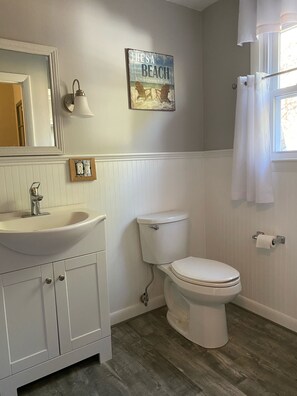 Een badkamer met een wit wastafelmeubel, toilet en wastafel. Boven de wastafel hangt een spiegel en aan de muur een afbeelding in een lijst.