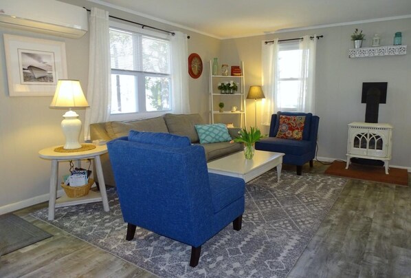 A living room with a sofa, armchairs, a coffee table, a side table with a lamp, a bookshelf, and a fireplace.