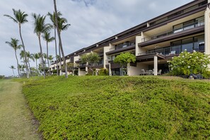 Un hotel de varios pisos con balcones, césped cuidado y palmeras.