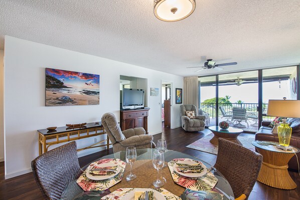 Amplia sala de estar con comedor, televisor y balcón con mobiliario exterior.