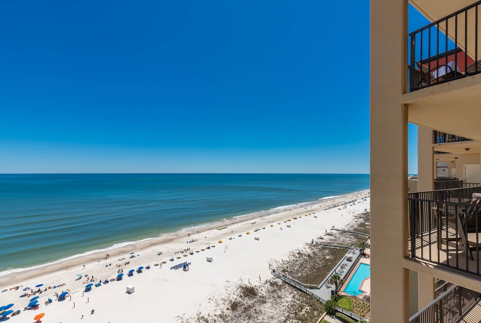 A beach view from a balcony with a pool and beach umbrellas.