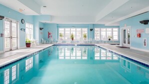 Ein großes Hallenbad mit klarem, blauem Wasser, umgeben von hellblauen Wänden und weißen Stühlen.