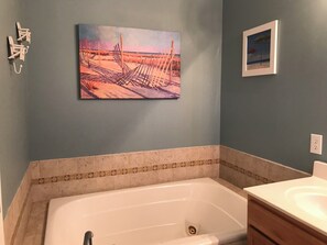 Un baño con bañera, lavamanos y un cuadro de una playa.