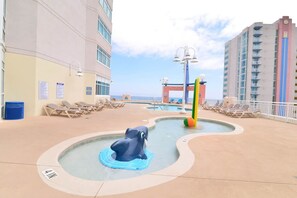 A pool area with a lifeguard stand, lounge chairs, and a building with multiple floors.