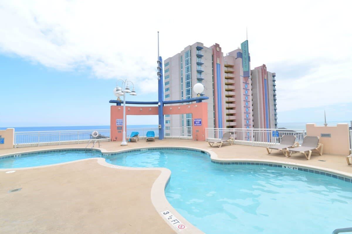 A pool area with a view of the ocean, a building with multiple balconies, and lounge chairs.