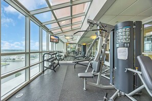 A gym with exercise equipment and a large window overlooking a body of water. - Prince Luxury Ocean View w Sky Pool Lazy River (North Myrtle Beach)