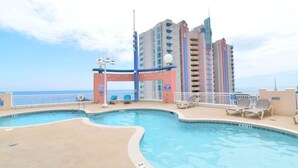 A pool area with a view of the ocean, a multi-story building in the background, and lounge chairs. - Prince Luxury Ocean View w Sky Pool Lazy River (North Myrtle Beach)