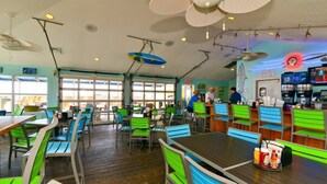 A restaurant with green and blue chairs, wooden tables, and ceiling fans. - Prince Luxury Ocean View w Sky Pool Lazy River (North Myrtle Beach)