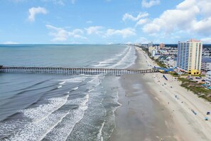 Une plage avec une jetée qui s’avance dans l’eau, bordée d’une rangée d’immeubles dotés de balcons donnant sur la plage.