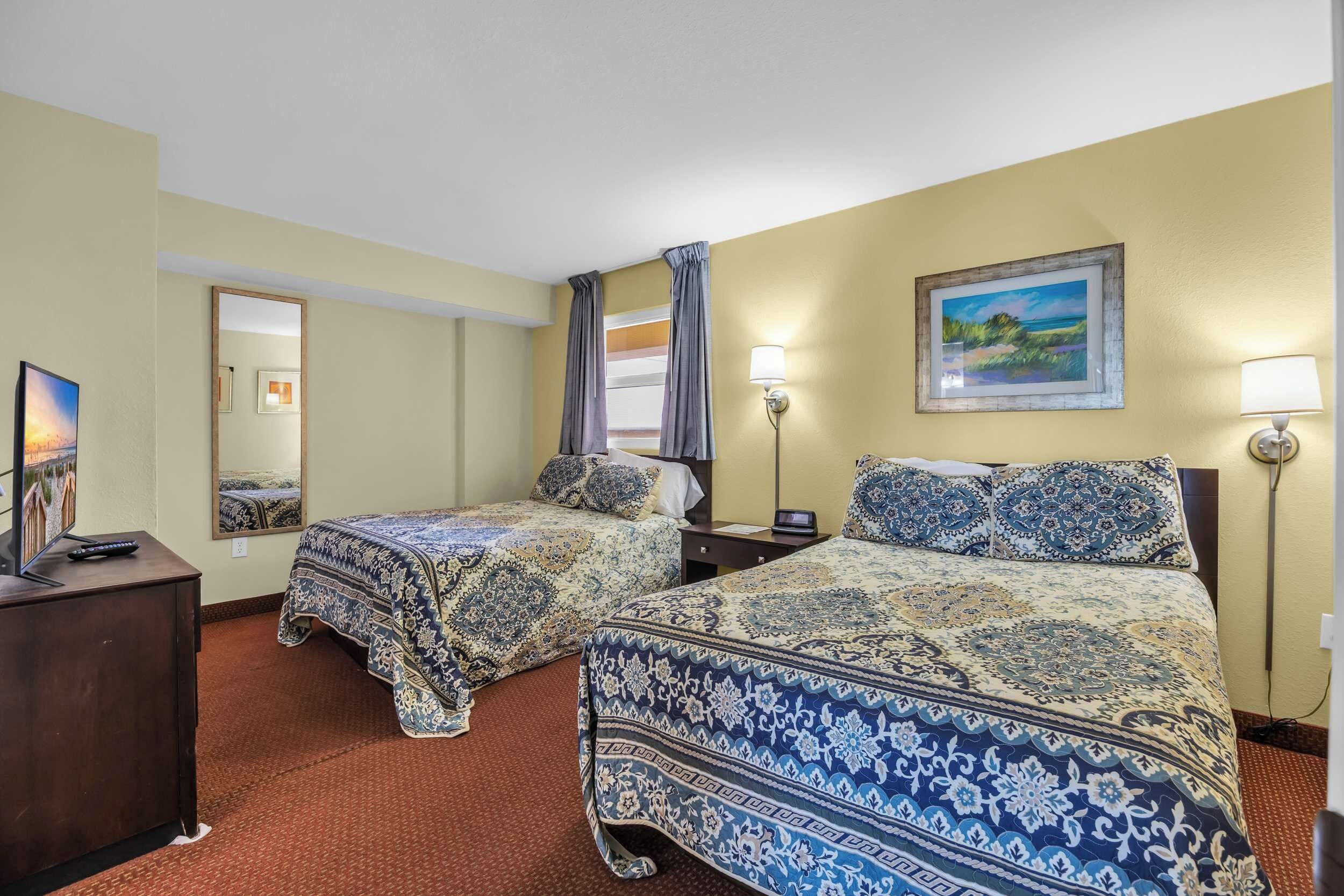 A hotel room with two beds, a desk, a mirror, and a painting on the wall.