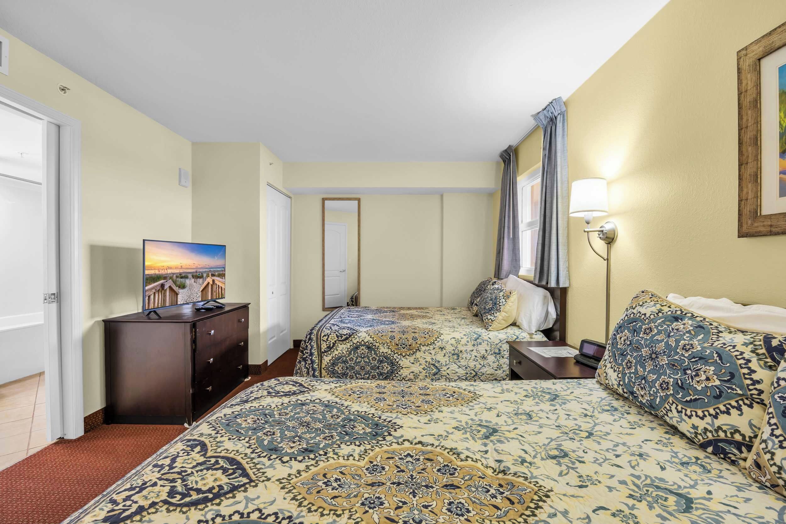 A hotel room with two beds, a TV, a dresser, and a lamp.