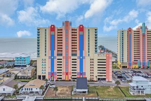 A multi-story hotel with a central tower, a parking lot, and a view of the ocean.