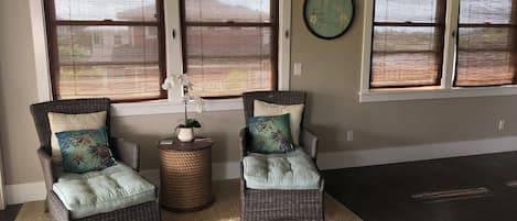 Una habitación con dos sillones de mimbre, una mesita de fibras naturales y un reloj de pared.
