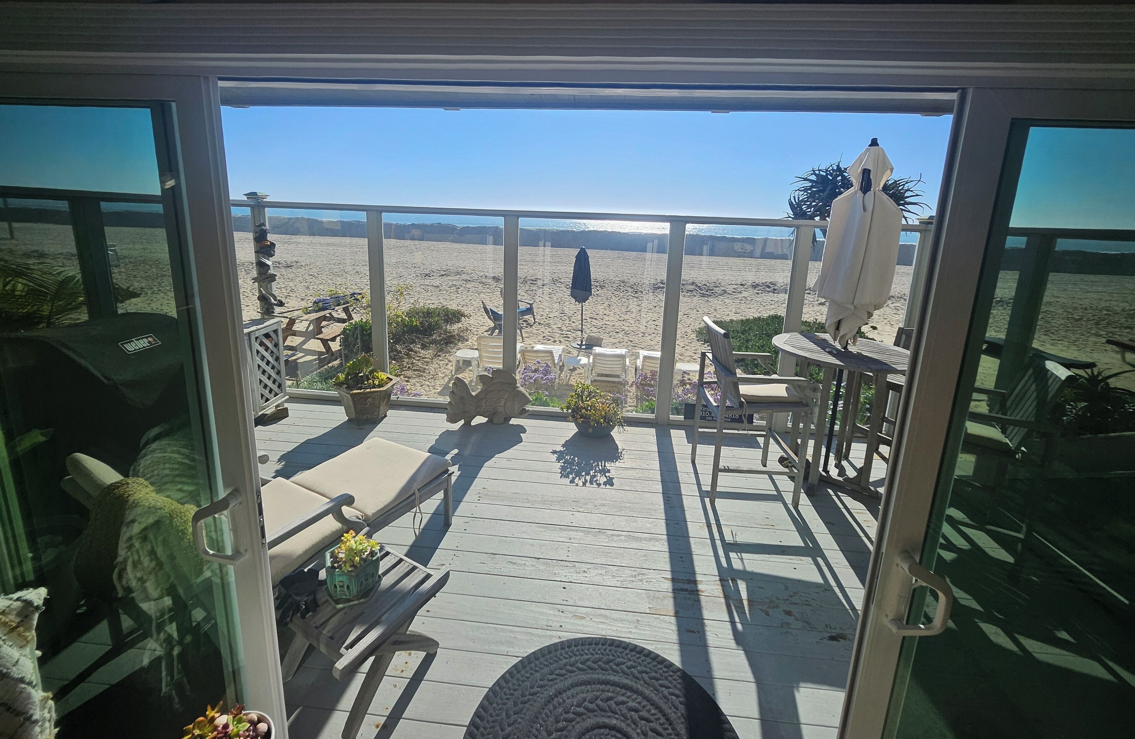 Eine Terrasse mit Gartenmöbeln, Blick auf den Strand und einem Geländer.