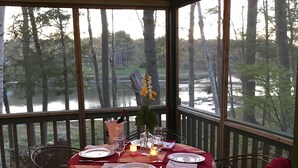 A dining area with a table set for two, overlooking a forested area and a body of water. - 600' of Waterfront Chauncey Creek House, fenced yard, office, walk to the beach (Kittery)
