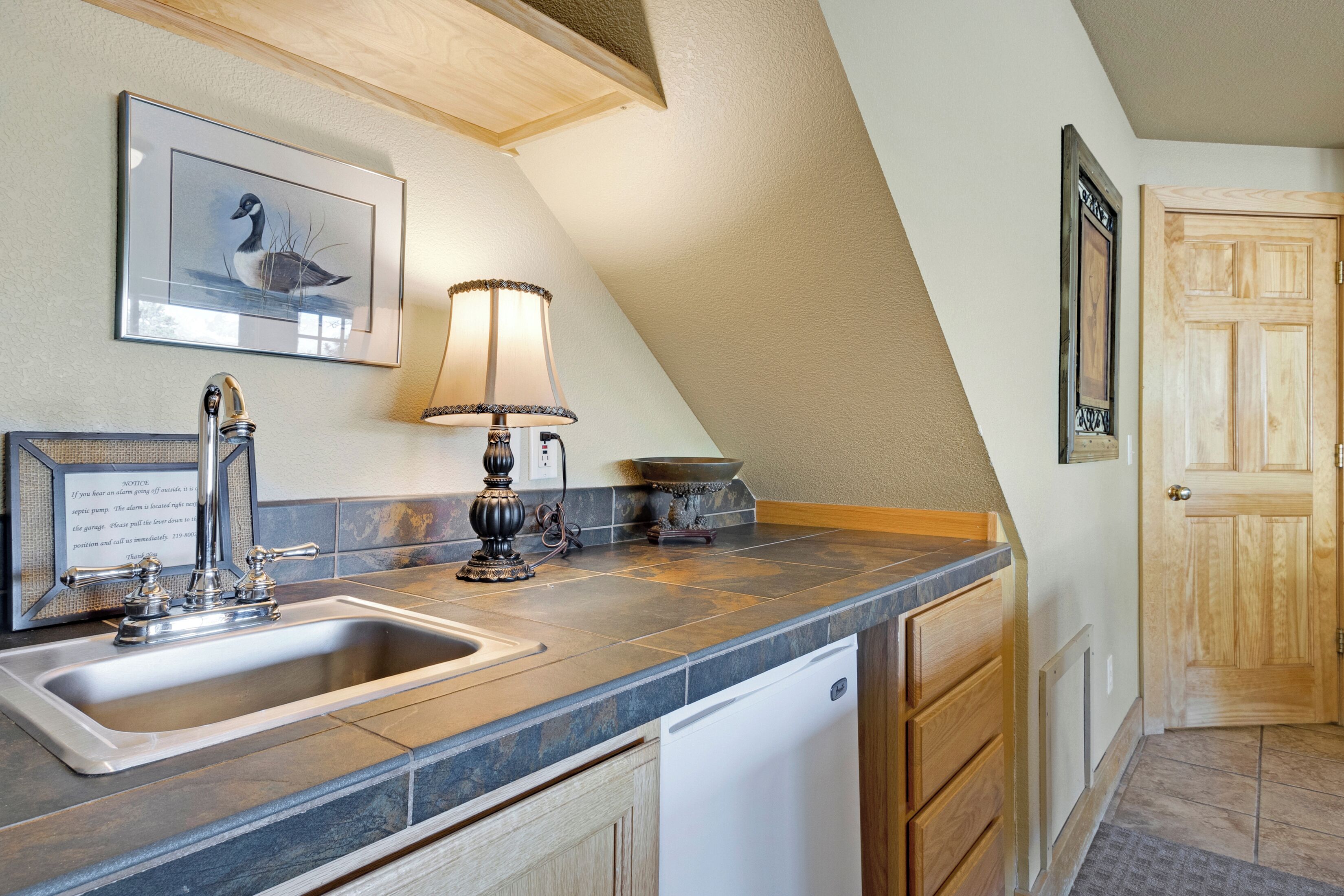 A kitchen with a sink, stove, and a lamp. There is a framed picture on the wall and a wooden door.