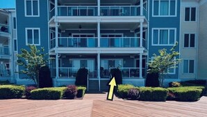 Un edificio residencial de varios pisos con balcones, una entrada central y un área de terraza de madera.