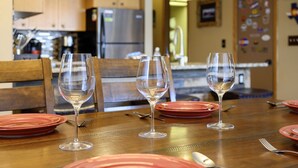 A dining table set with red plates and three wine glasses, with a kitchen in the background.