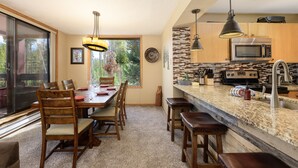 A modern kitchen with a large island, stainless steel appliances, and a dining area with wooden chairs and a glass table.