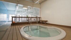 A hot tub in a spacious indoor area with wooden flooring and a high ceiling.