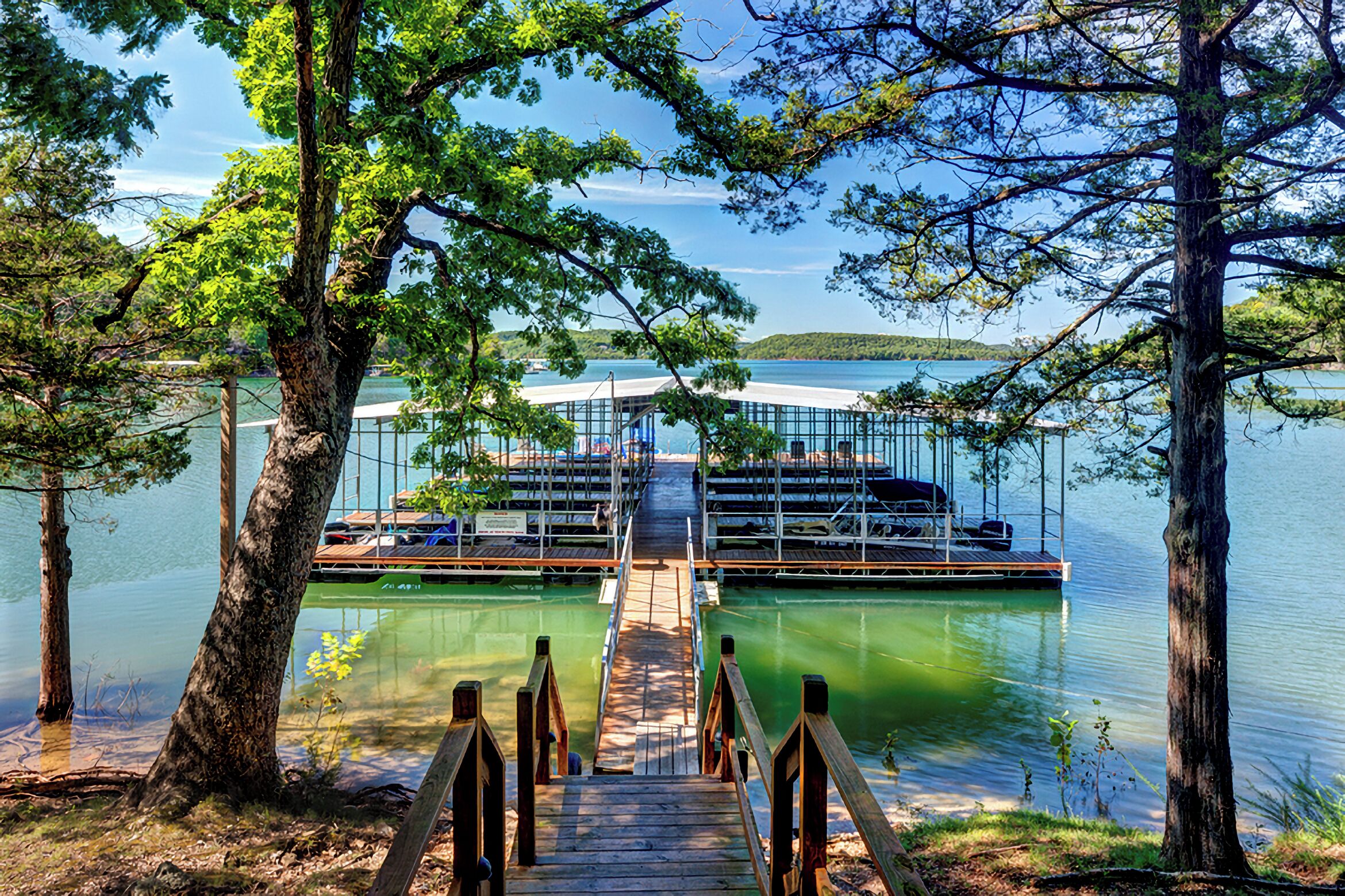 A dock leading to a glass-enclosed building with a view of a lake and distant hills.