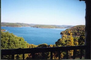 Ein See, umgeben von bewaldeten Hügeln, Blick vom Balkon mit Geländer.