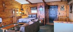 Ein gemütliches Blockhaus-Zimmer mit einem Bett, einer Bank, einem kleinen Tisch und einer Holztür.