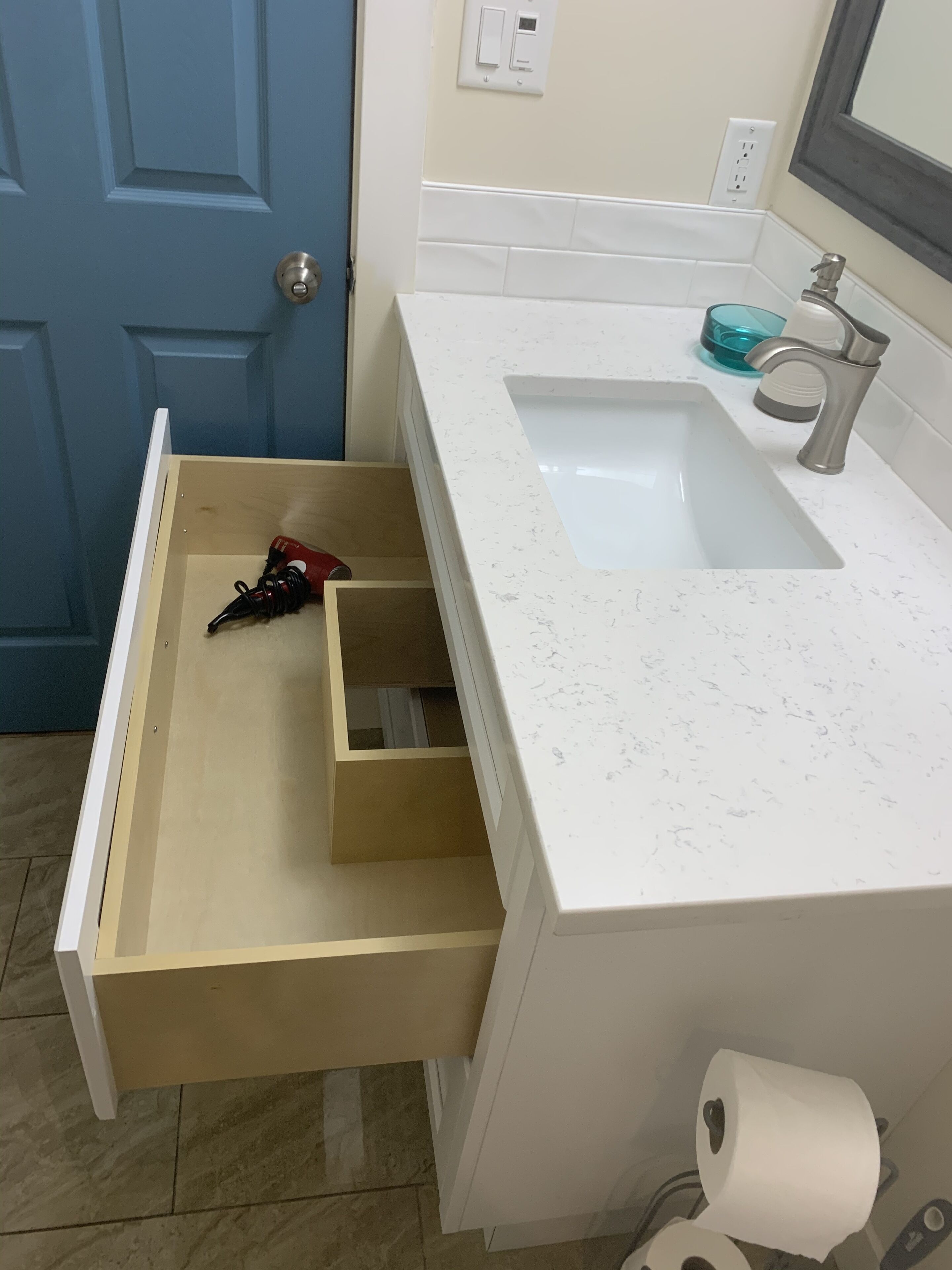 Un baño con un lavamanos blanco, un espejo y una puerta azul.