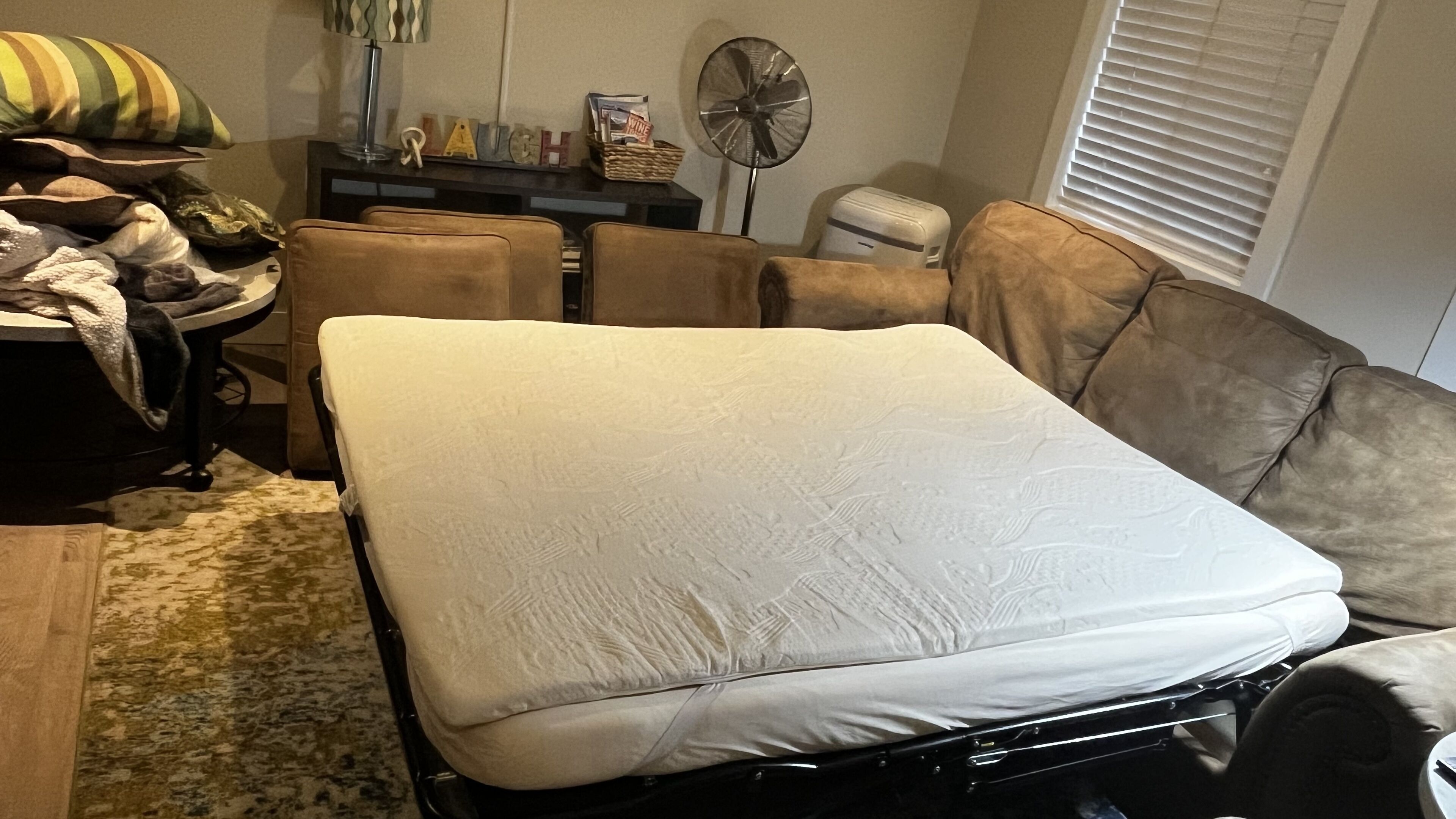 A compact living space with a bed, a small table, a fan, and a couch.