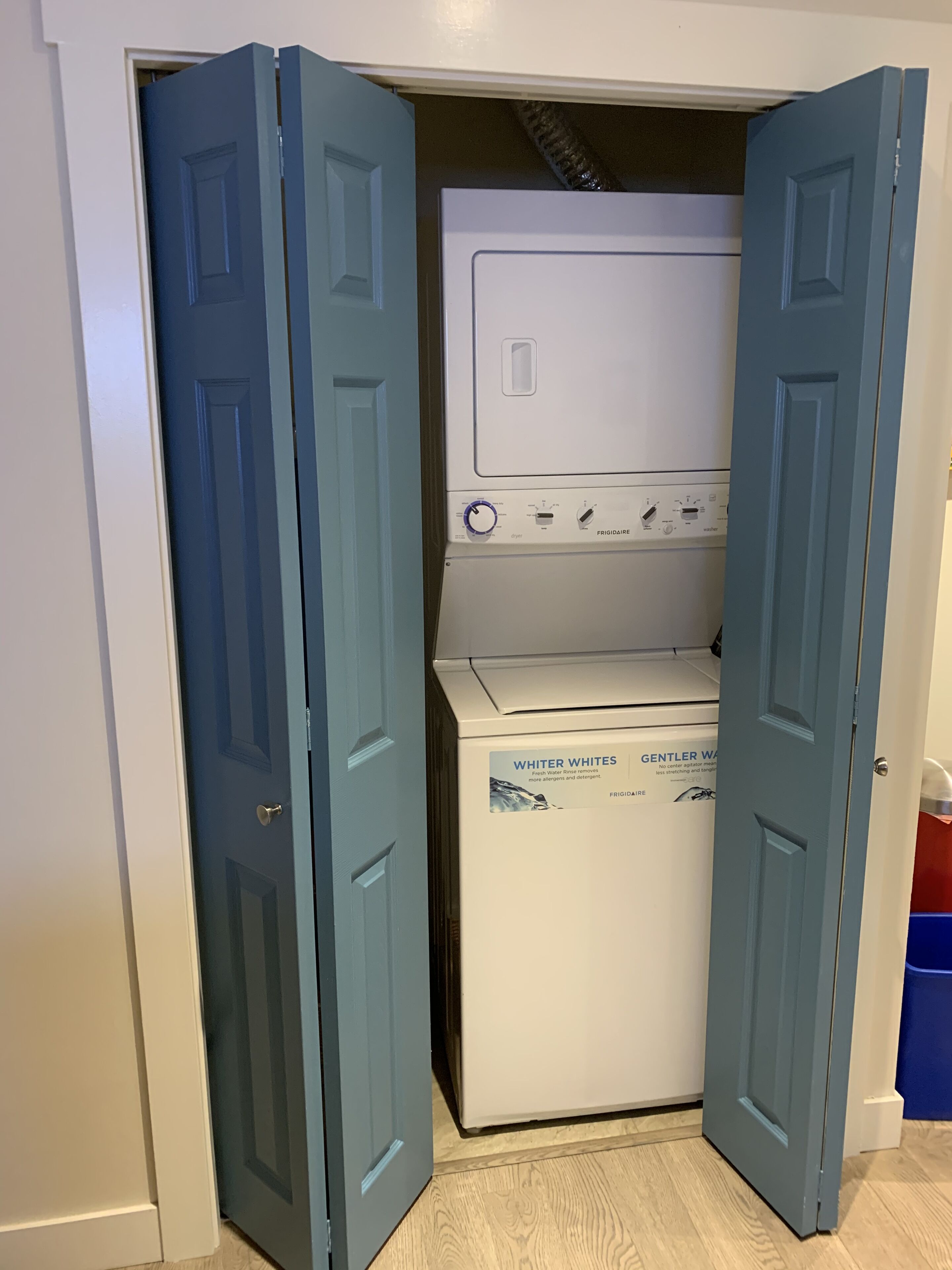 A laundry room with a front-loading washer and dryer, a blue door, and a blue bin.
