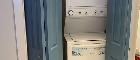 A laundry room with a front-loading washer and dryer, a blue door, and a blue bin.