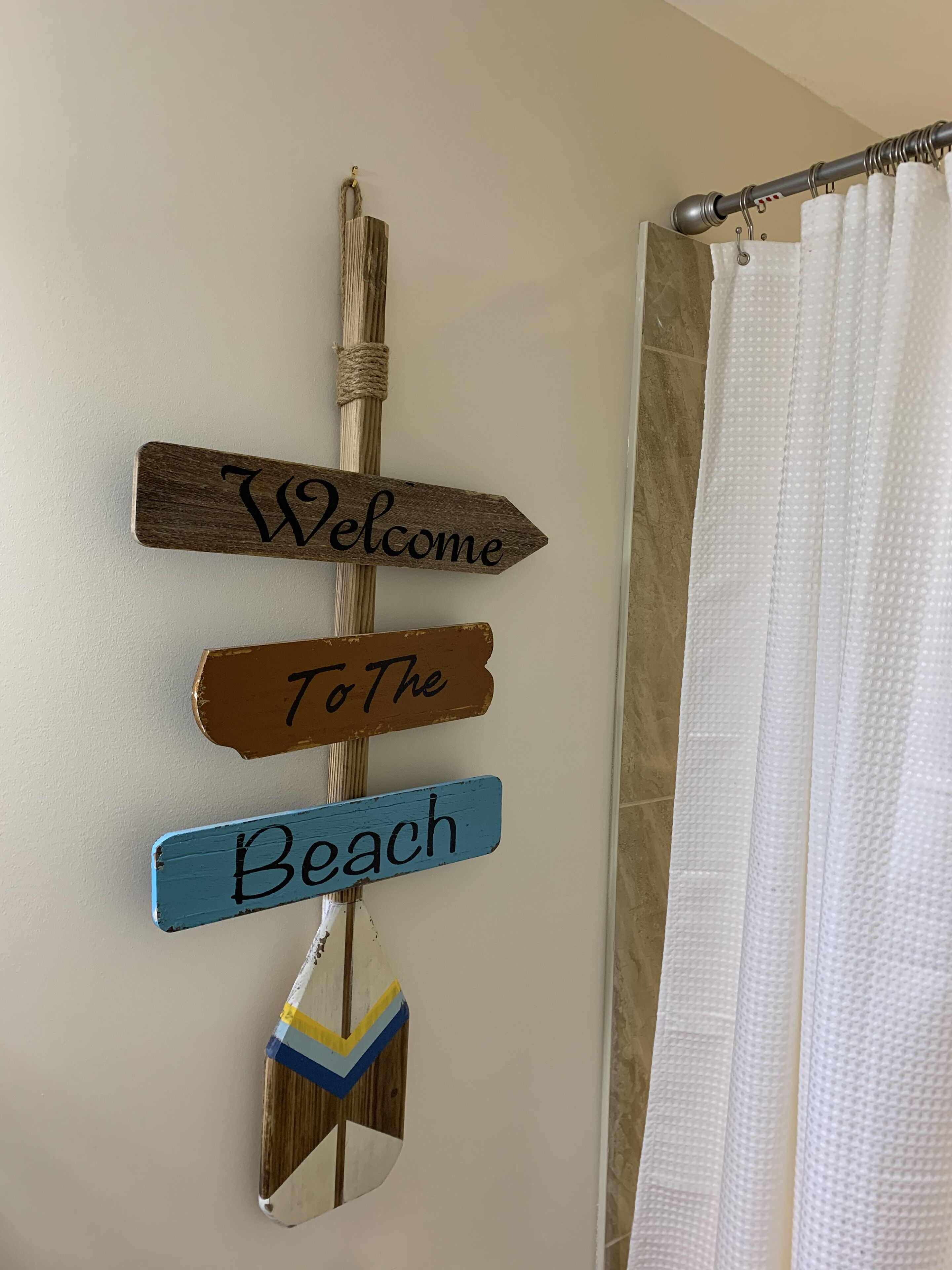 A wall with three wooden signs reading "Welcome," "To The," and "Beach," and a beach-themed mirror.