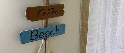 A wall with three wooden signs reading "Welcome," "To The," and "Beach," and a beach-themed mirror.