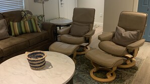 Un salon avec un canapé en cuir marron, deux fauteuils inclinables, une table basse ronde et un tapis à motifs.