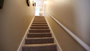 A carpeted staircase with a handrail, leading to a room with a door at the top.