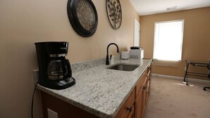 A kitchen with a granite countertop, a coffee maker, a sink, and a window with blinds.
