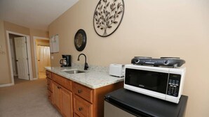 A compact kitchen with a microwave, toaster, and coffee maker on the counter, wooden cabinets, and a decorative wall piece.