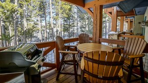 Terraza de madera con una parrilla y sillas, con vistas a un bosque.