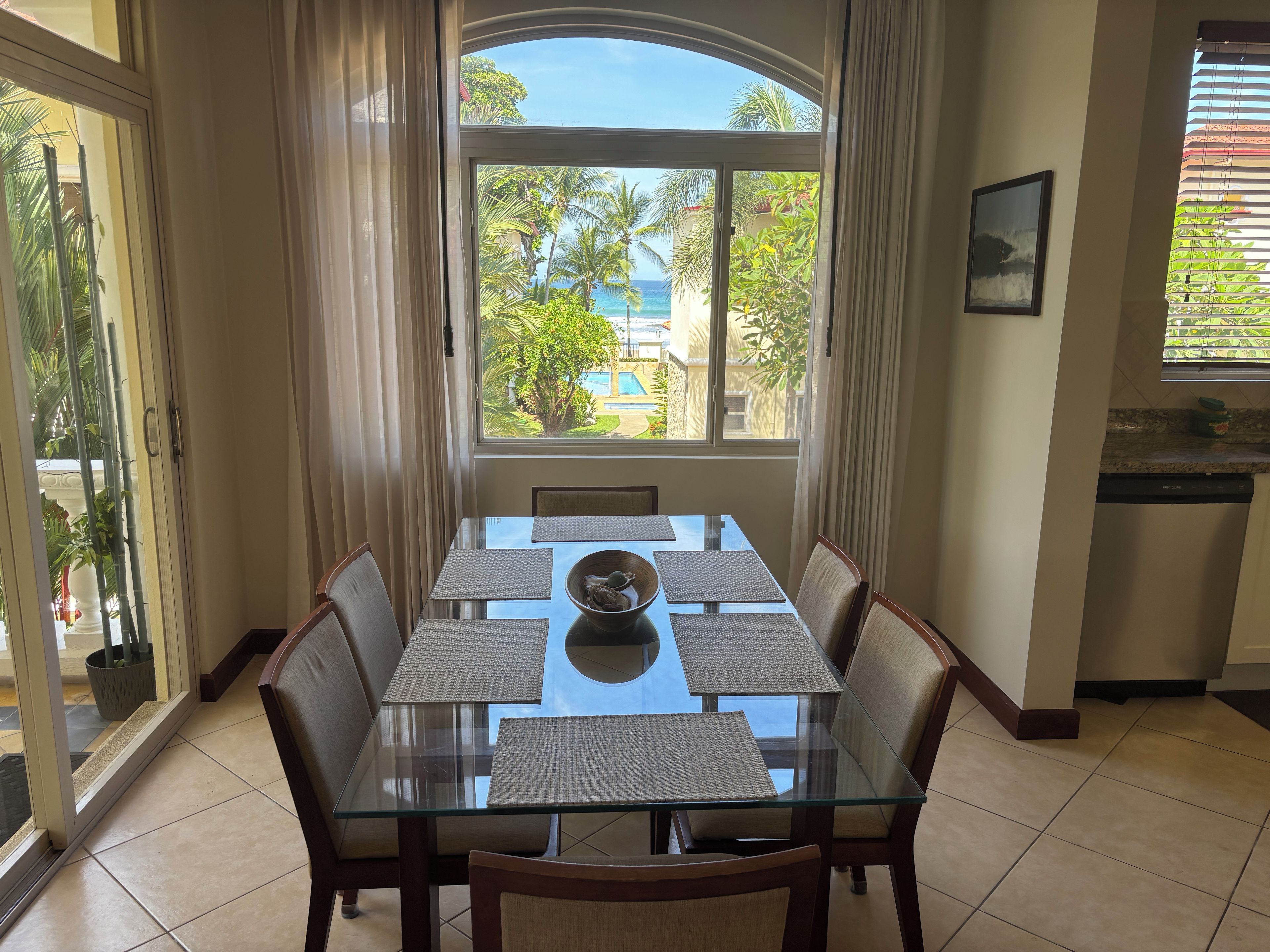 A dining area with a glass table, chairs, and a view of the ocean through large windows.