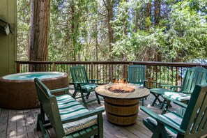 Eine Holzterrasse mit grünen Stühlen und einem runden Tisch mit einer Feuerstelle.