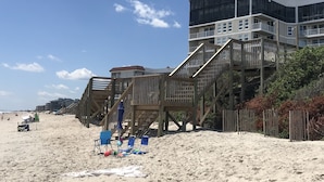 A beachfront property with a wooden deck, multiple balconies, and a sandy beach area with beach chairs and umbrellas. - Perfect condo for your getaway.  (N Topsail Beach)
