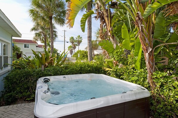 A hot tub in a lush garden with palm trees and a house in the background. - House & Cottage: Sleeps 8 Drive to your door, Patio, Hot Tub, Grill & Wifi (Clearwater Beach)