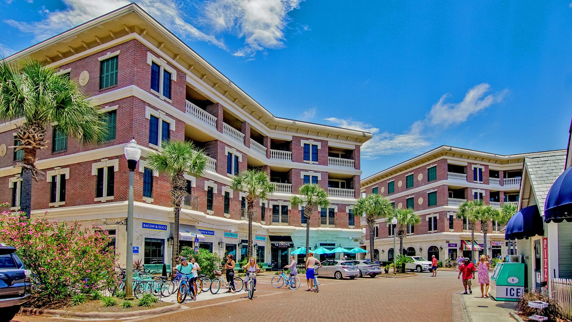 A multi-story hotel with a brick facade, balconies, and a street in front with pedestrians and parked cars.