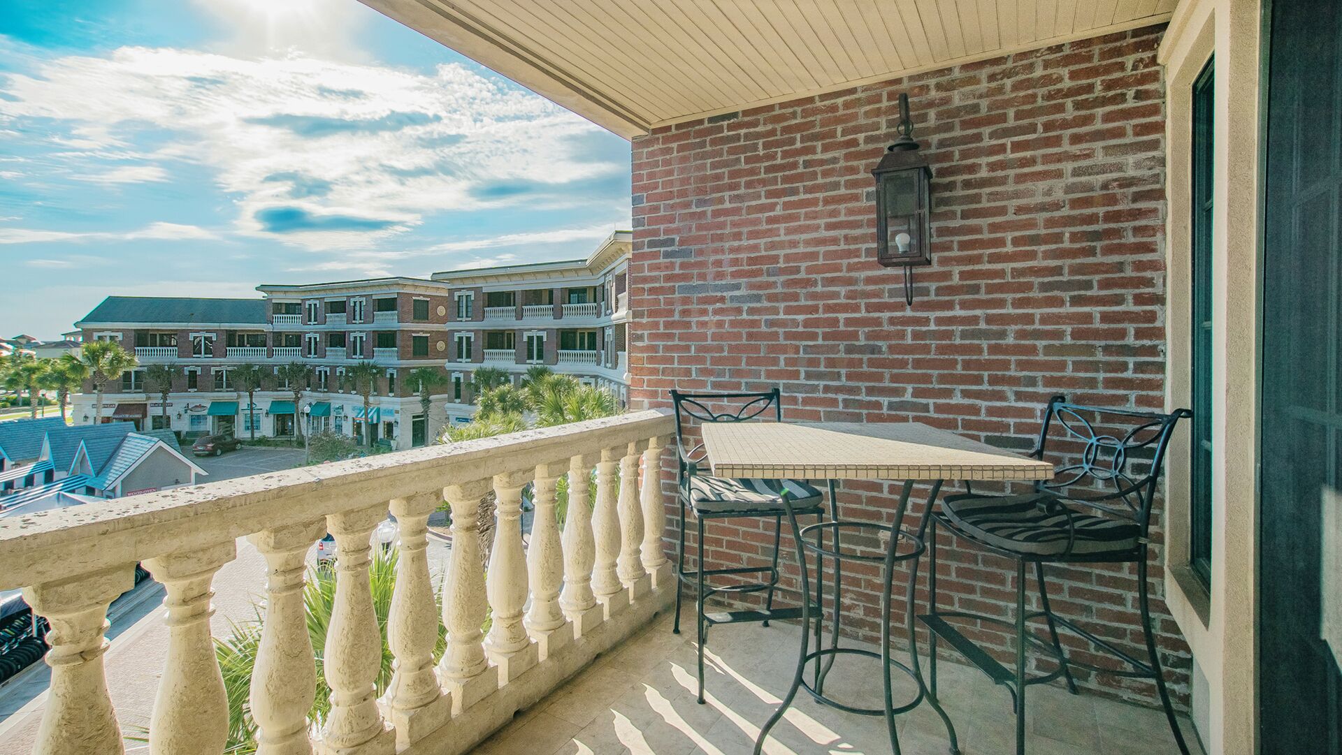 A balcony with a table and chairs, a brick wall, and a view of a multi-story building with balconies.