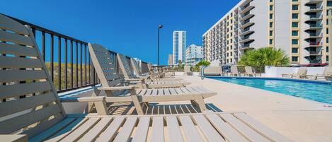 A poolside area with sun loungers and a pool, surrounded by high-rise buildings.