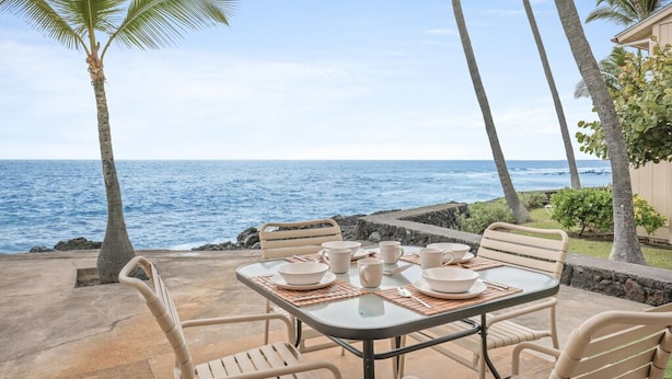 Un espace extérieur aménagé pour les repas, avec une table dressée pour quatre personnes, donnant sur l’océan.