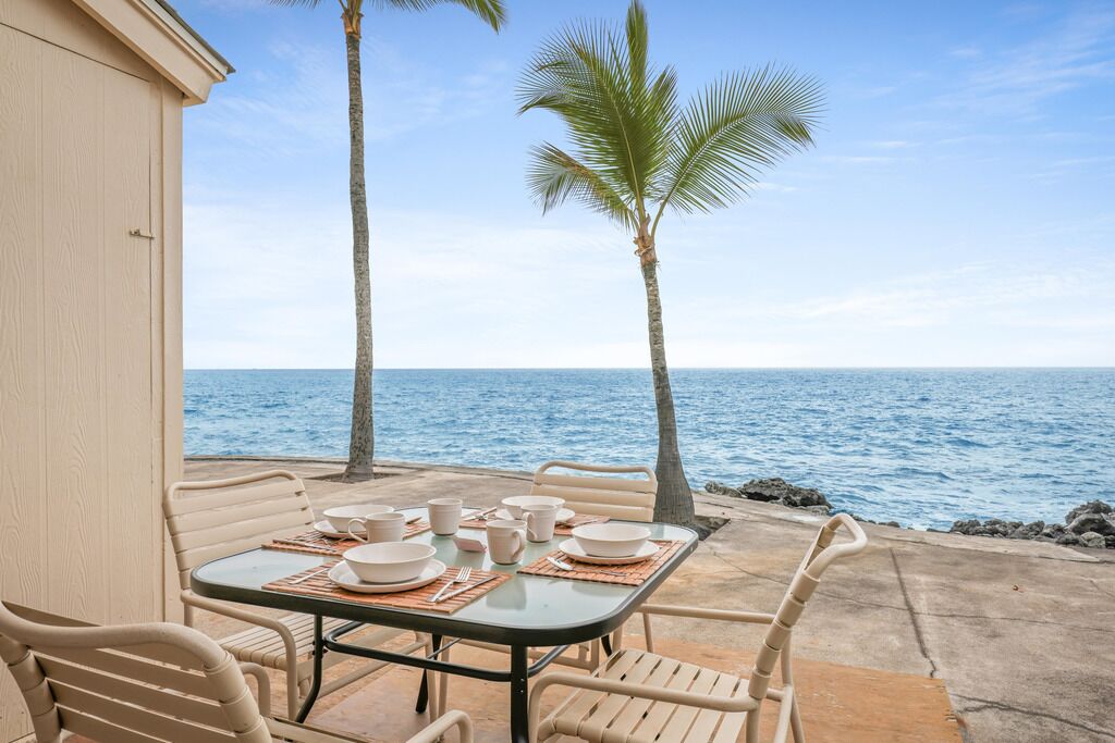 Une table dressée pour le dîner, avec vue sur l’océan, les palmiers et un bâtiment en arrière-plan.