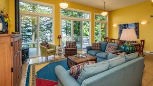 A spacious living room with a large sofa, two armchairs, a coffee table, and a fireplace. There are large windows providing a view of the outdoors. - Orcas Island, Casa Verde #269 (Eastsound)