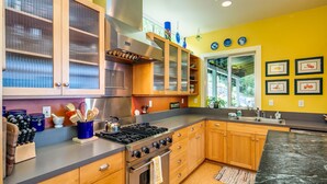A modern kitchen with wooden cabinets, a stainless steel range hood, and a large island with a sink. - Orcas Island, Casa Verde #269 (Eastsound)